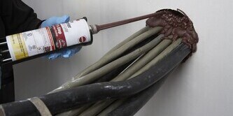 Applying 3M fire barrier sealant around cables in a wall penetration.
