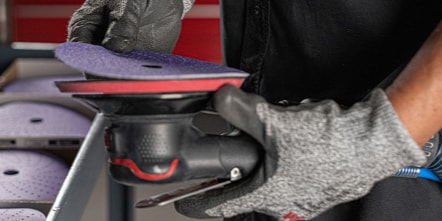 Person placing a 3M&trade; Cubitron&trade; II disc on a back up pad with other abrasives in background.