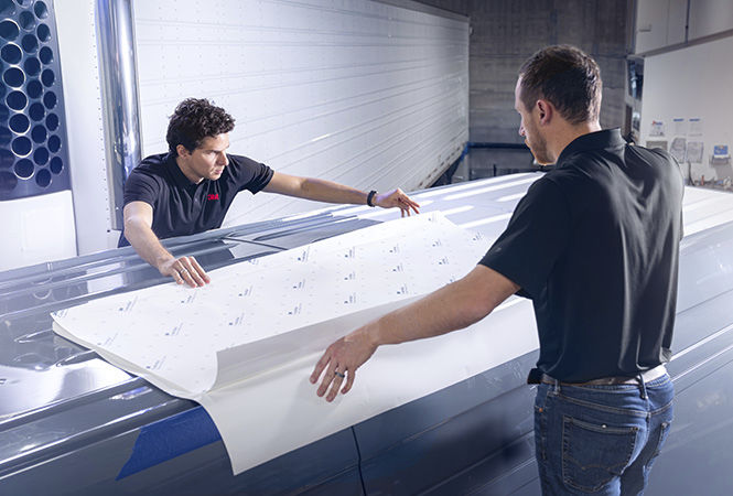 Technicians applying 3M film to the rooftop of a vehicle inside a service bay.

