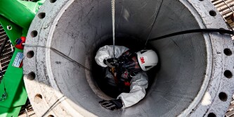Industrial worker wearing safety gear and a supplied‑air respirator while performing confined space entry inspection.
