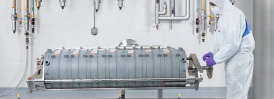 A pharmaceutical worker in full personal protective equipment, opening a tank of material.
