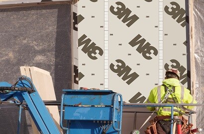 Person in a construction vehicle basket applies siding to a building under construction