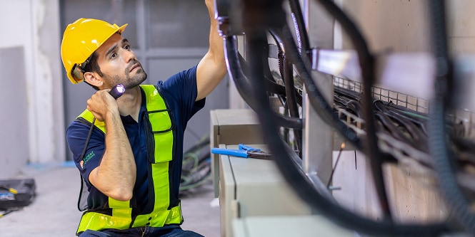 worker in safety gear inspecting electrical cables with flashlight
