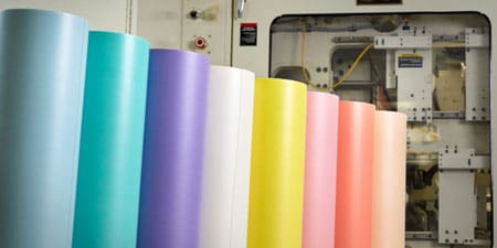 A row of colorful 3M flexographic mounting tape rolls standing vertically in a factory setting.
