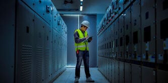 Worker in a hard hat and safety vest inspecting equipment in a data center
