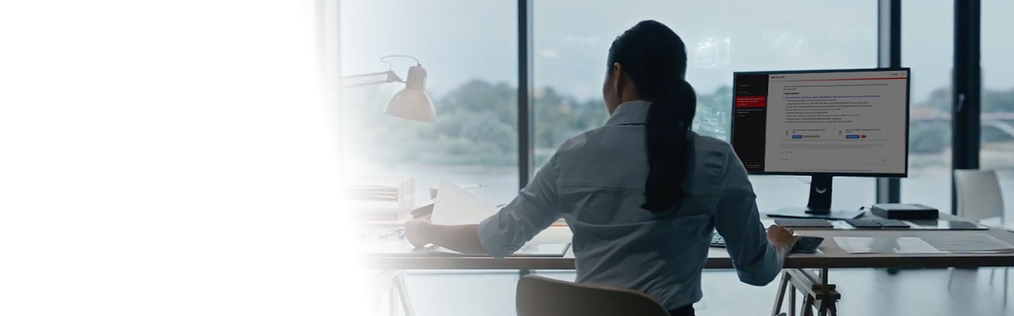 Employee working at a desk, viewing a 3M Policy Central page on a desktop monitor in a modern office.