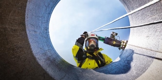 Safety technician in full protective gear performing confined‑space entry using 3M fall protection equipment.
