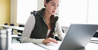 A woman sits on a laptop in a brightly lit classroom which uses 3M window film to reduce sun glare.
