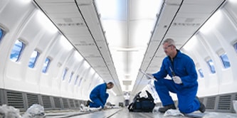 Two people working inside the airframe of a plane.
