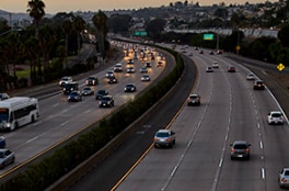 A busy eight-lane highway at dusk has easily viewable pavement markings.