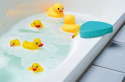 Rubber ducks in a bathtub with a Scotch-Brite&reg; Swift Scrub Bathroom Buildup Remover on the edge of the tub.