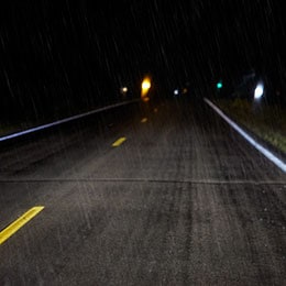 A two-lane highway in the dark and the road has yellow lines that are brightly illuminated by headlights showing enhanced visibility in harsh weather.