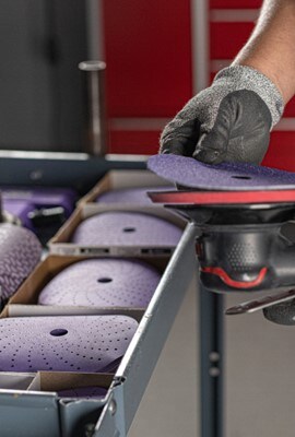 Someone applying a purple abrasive disc to a random orbital sander with organized abrasives in the background.