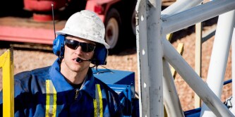 Industrial worker wearing protective headset, helmet, and safety gear operating equipment at a worksite.
