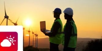 Silhouetted wind energy workers using a laptop at sunset near a wind farm, featuring a sun and cloud weather icon.
