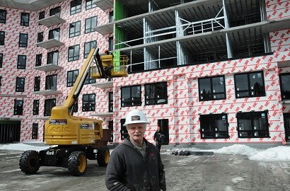 A man in a hard hat stands in front of a building under construction with product siding visible