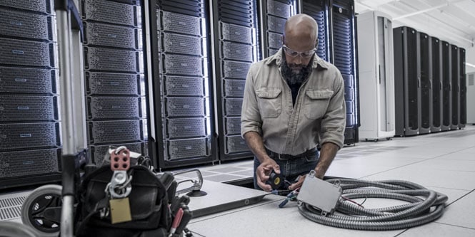 worker installing electrical cables in subfloor of data center
