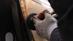 A gloved hand using a handheld abrasive tool on a metal surface, generating sparks
