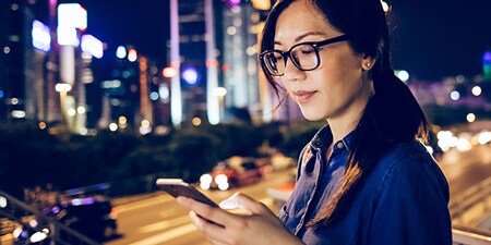 Woman using her mobile device in a city at night.
