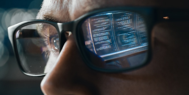 image of person looking at data with the screen reflected in his glasses
