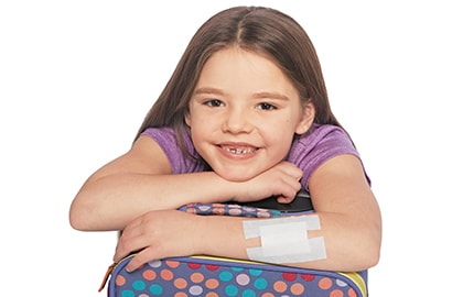 Girl hugging her backpack with Nexcare&trade; Gentle Paper Tape bandage on her arm.