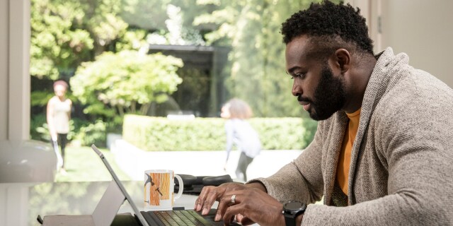 Man working on a laptop beside a large window. 
