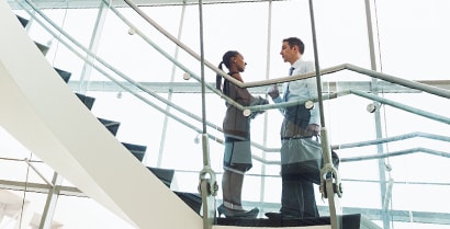 A professionally dressed man and woman talk on a stairway surrounded by floor-to-ceiling windows covered in 3M solar window film.
