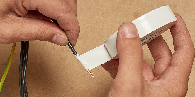 worker wrapping wire in white electrical tape
