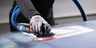 collision tech using sander on car panel for fine sanding before primer
