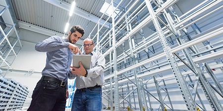two men collaborating in a warehouse looking at ipad
