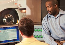 Man sitting on a person's desk looking at three screens.