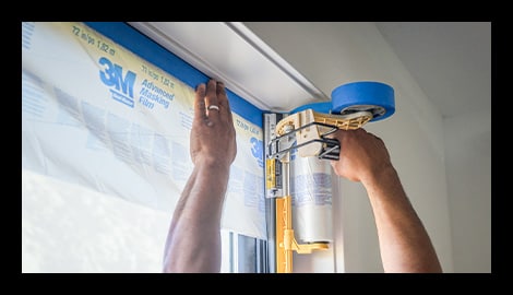 Contractor using a 3M Hand-Masker M3000 dispenser with 3M Advanced Masking Film to mask a window frame before painting.