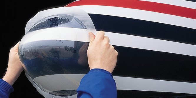 Technician applying 3M polyurethane radome boot to an aircraft nose cone for surface protection and erosion resistance.
