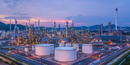 Large industrial refinery complex at dusk with storage tanks, towers, and illuminated structures.
