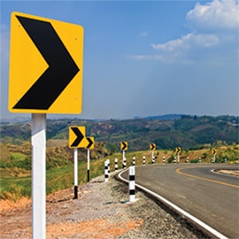 Advanced reflective sign technology on chevron traffic signs line the side of a road with a horizontal curve.
