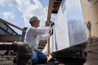 A person wearing a hard hat applies insulation to the side of a building
