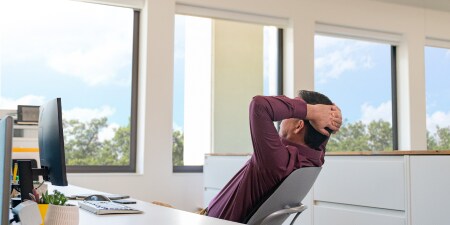 man relaxes at desk and looks out window
