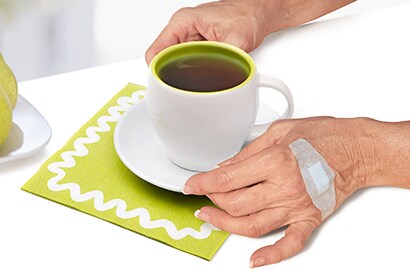 Hand with Nexcare bandage on it while holding a cup of coffee.
