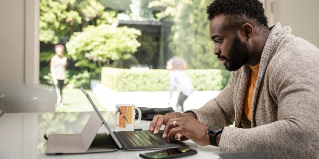 Man working on a laptop beside a large window.
