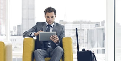A business man comfortably sits working on a tablet in a hotel lobby that uses sun blocking window film.
