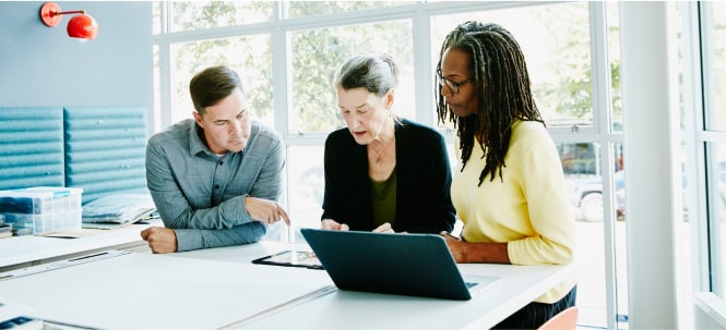 Three individuals are gathered around a white table in a collaborative discussion.
