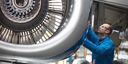 An employee inspecting the external shell of a jet turbine.
