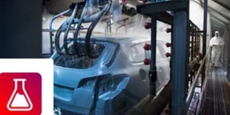 A car body passing through an automated manufacturing wash or spray booth, featuring a chemical beaker icon.
