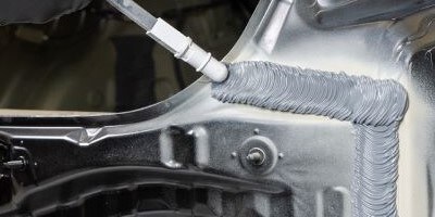 A grey seam sealer bead being applied to the body of a car.