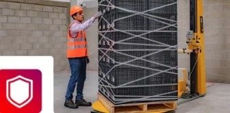 A worker in a safety vest secures a large pallet of stacked crates with heavy-duty strapping, featuring a shield icon.
