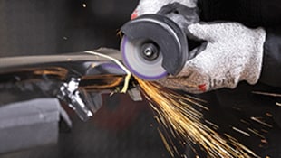 A gloved hand operating a rotary grinding tool on metal, creating bright sparks during grinding
