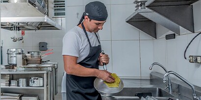 male chef using a 3M pad to clean in a commercial kitchen
