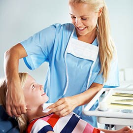 Female dental assistant examining young patient in dental chair.
