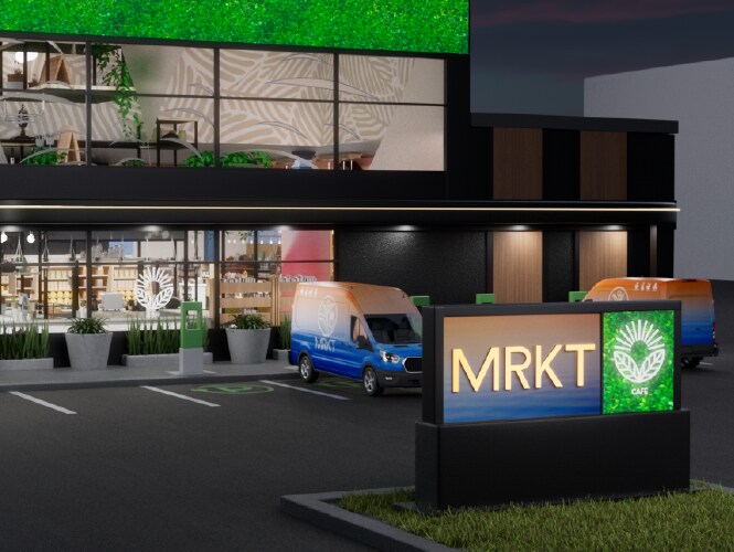 Storefront with illuminated signs and parking area, showcasing a green wall and delivery vans.
