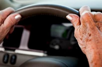 The hands of an elderly driver grasp a steering wheel